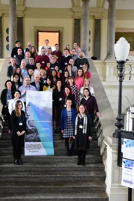 Photo of a group of 20+ researchers standing inside on a grand stone staircase holding a large poster