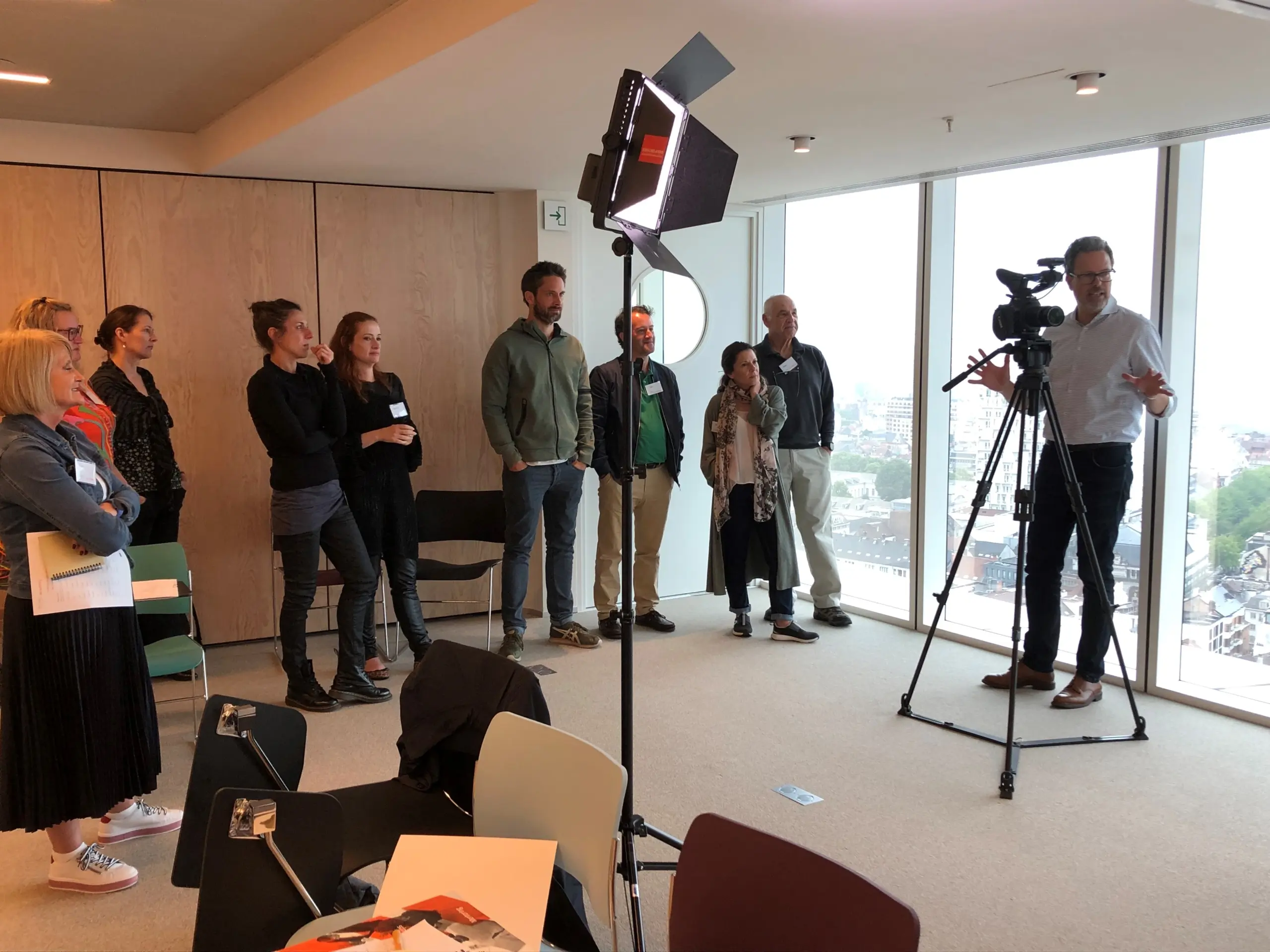 A man behind a large TV style camera explaining something to a group of 10 people