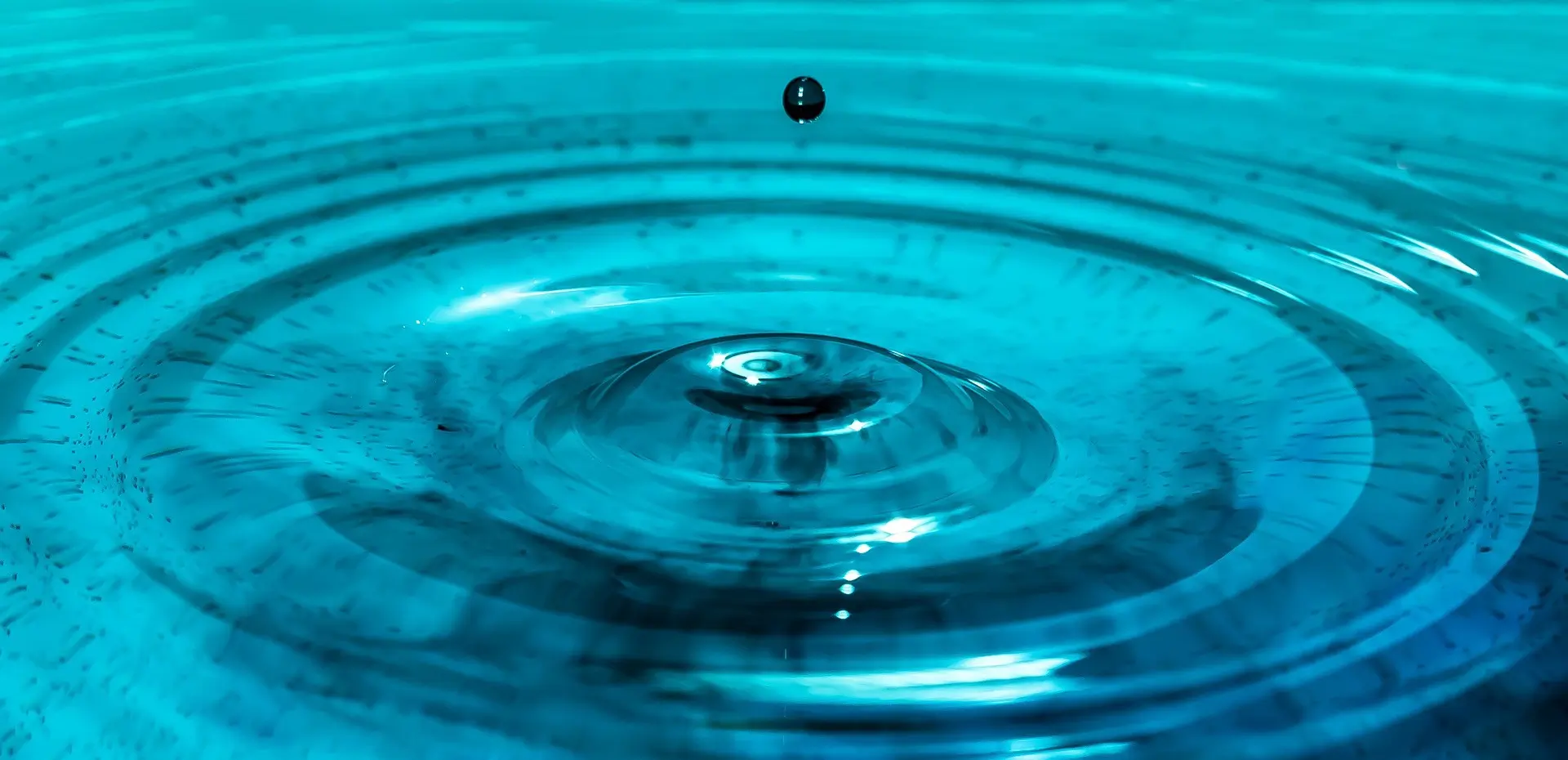 Photo of a water droplet hitting a pool of water and creating ripples