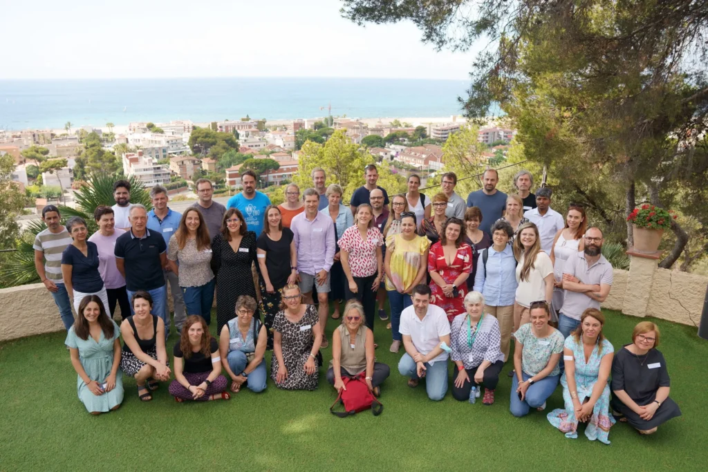 Group photo of 40 people outside a in Barcelona, surrounded by green and trees with the sea just visible in the background