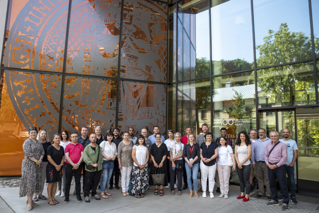 Group photo of 50+ researchers standing outside a modern glass-fronted building