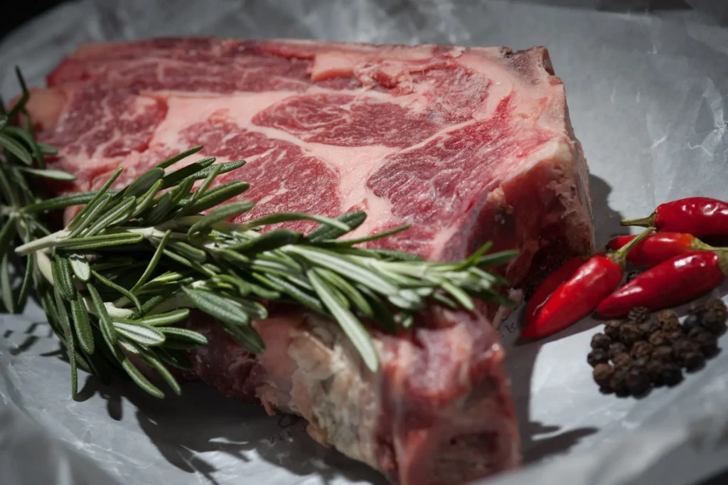 Large raw steak with a sprig of rosemary on top 