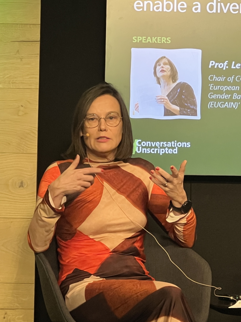 Woman sat on a stage with a microphone giving a speech