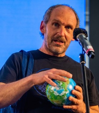man with grey hair holding a globe behind a microphone