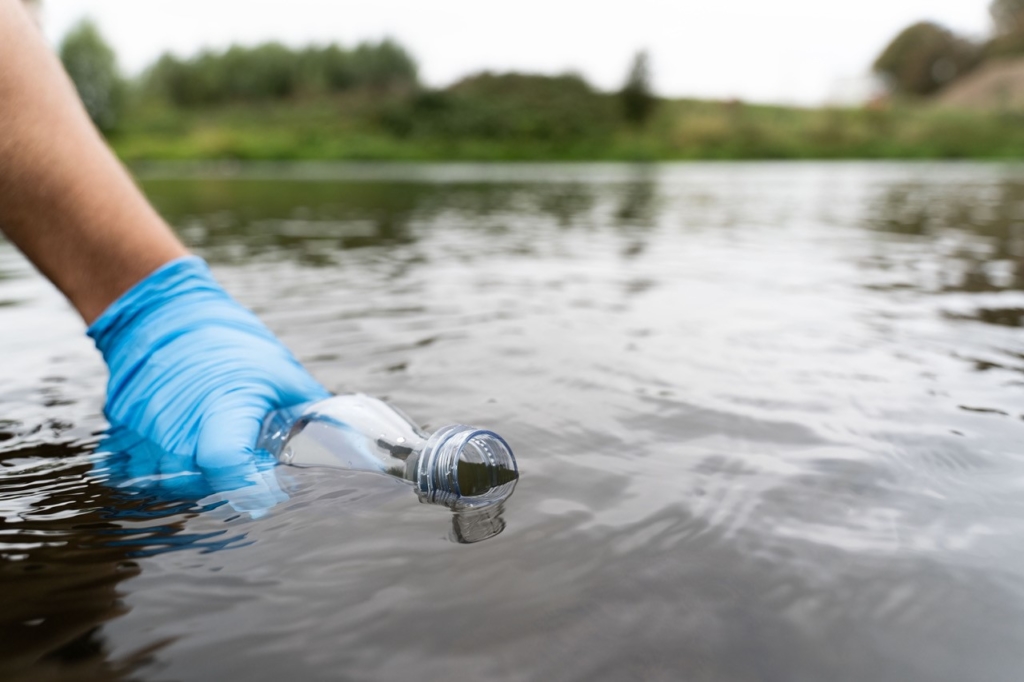 hand in a blue rubber glove taking a water sample from a pond