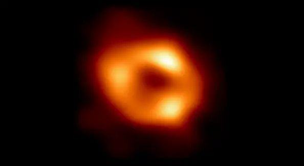 Photo of a black hole - a red/orange donut shaped ring with spots of white light with a black center