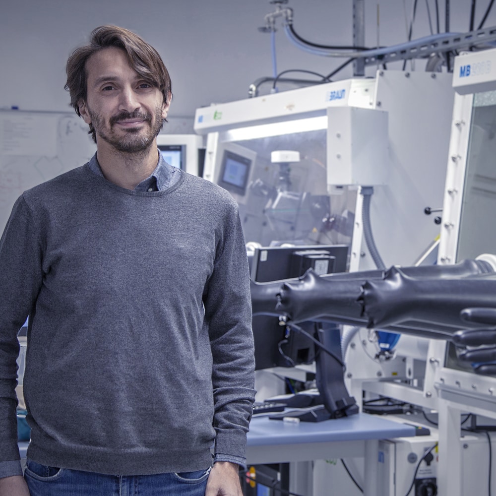 A young man in a grey sweater is standing in a laboratory.