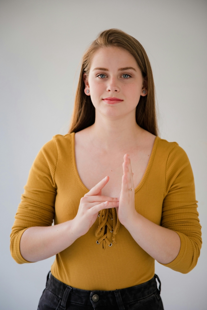 A young blonde woman with long hair who is using sign language.